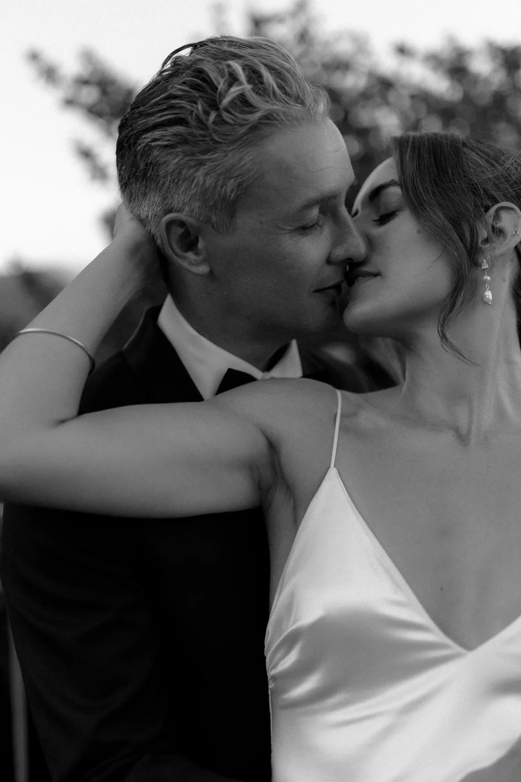 Home 21 A black-and-white photo of a couple embracing closely. The woman, wearing a satin dress, gently holds the mans neck while he wears a suit. They appear to be about to kiss, expressing affection and intimacy.