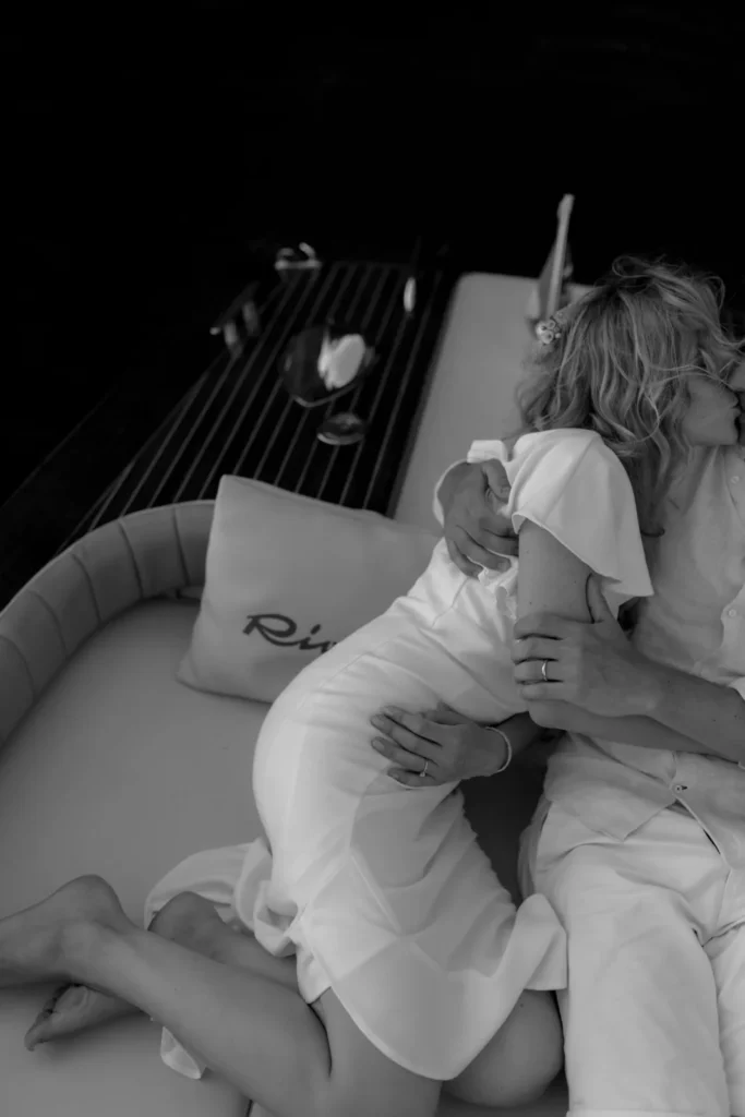 Kind Words 11 A couple shares an intimate moment on a boat, both dressed in white. The womans blonde hair is tousled, and they both wear rings.